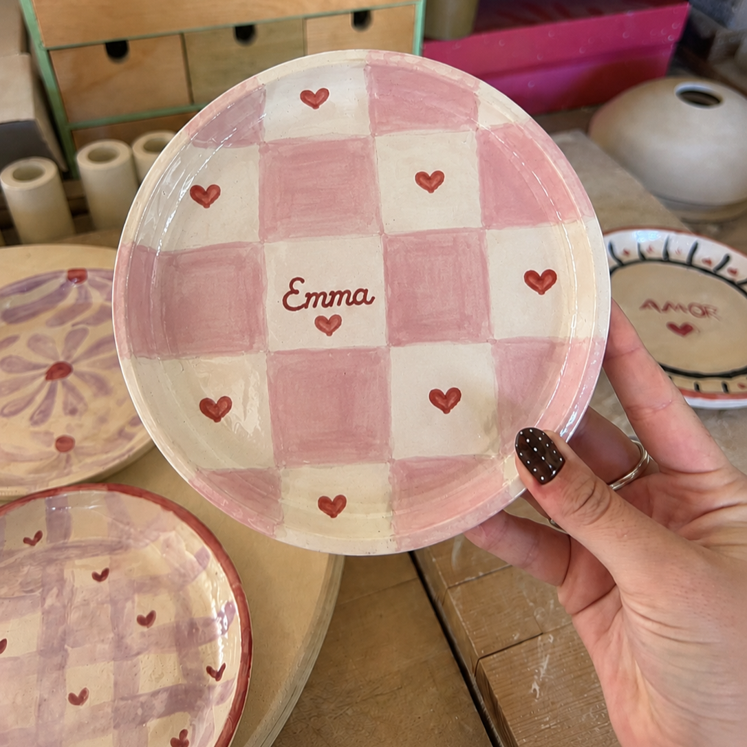 Pink checkered ceramic trinket dish being hand painted with Emma name